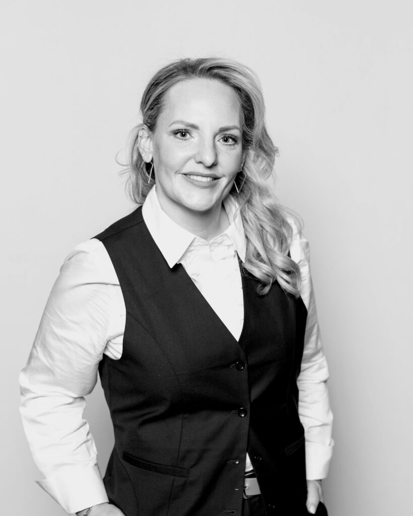 Black-and-white portrait of a smiling woman in a white shirt and black vest.